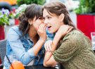 Two female friends sitting in a sidewalk cafe. They are whispering and gossiping.