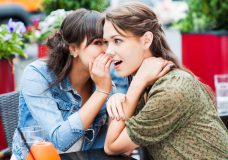 Two female friends sitting in a sidewalk cafe. They are whispering and gossiping.