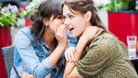 Two female friends sitting in a sidewalk cafe. They are whispering and gossiping.